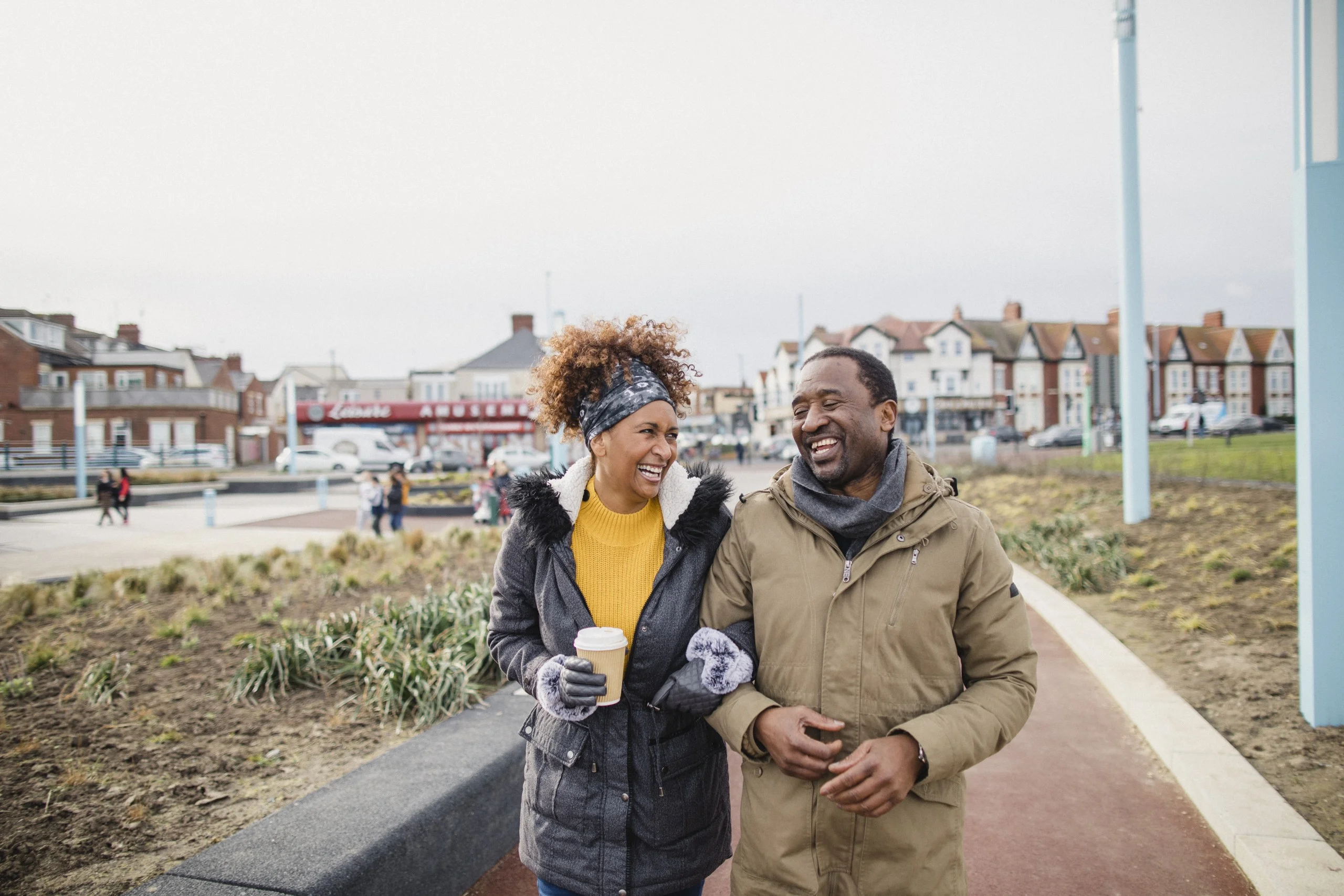 A couple walking arm-in-arm catching up over a coffee as they walk along a footpath.