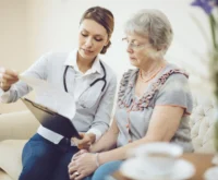 A healthcare professional sits with a patient, holding a document