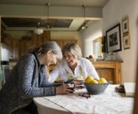 Two women sitting on chairs, laughing and enjoying a cup together