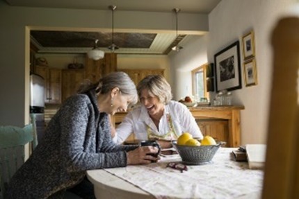 Two women sitting on chairs, laughing and enjoying a cup together