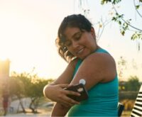 Person scanning continuous glucose monitor (CGM) with smartphone in park at sunset, promoting diabetes self-management and treatment adherence.