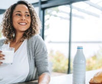 A women with a glass of milk smiling and looking outside the kitchen window