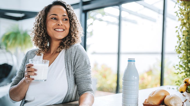 A women with a glass of milk smiling and looking outside the kitchen window